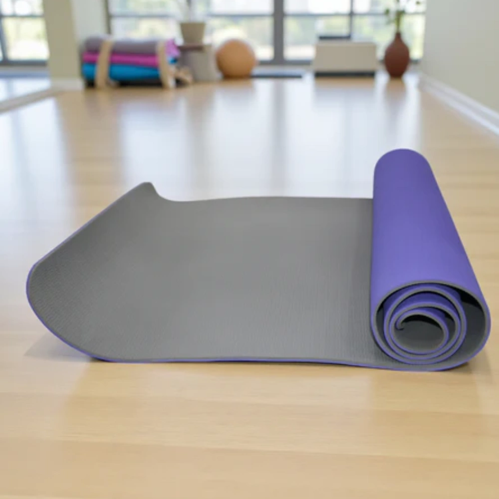A purple and grey dual-layer pilates mats partially unrolled on a wooden fitness studio floor.
