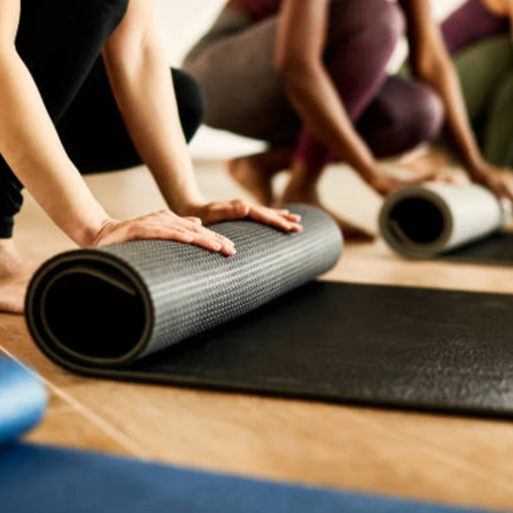 People unrolling durable black pilates mats in a fitness studio for a group workout session.
